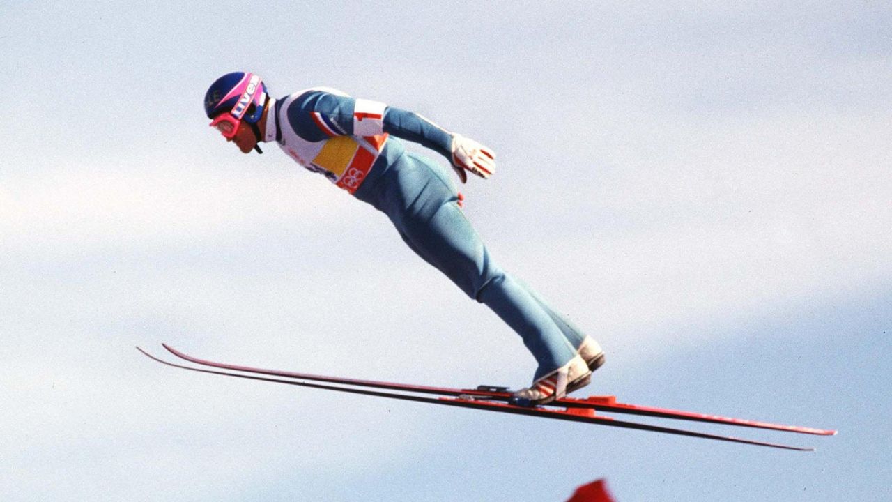 Ski jumper flying through the air during a jump at the 2026 Winter Olympics amid controversy over suit and aerodynamics rules